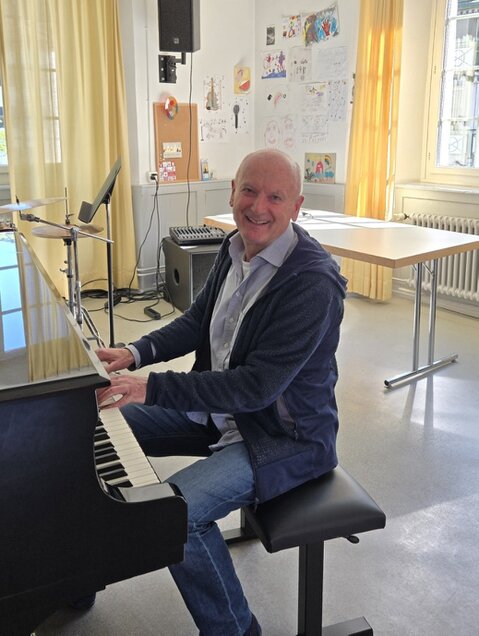 Pianist begleitet eine Gruppe älterer Menschen bei einer Bewegungsübung mit live gespielter Musik.