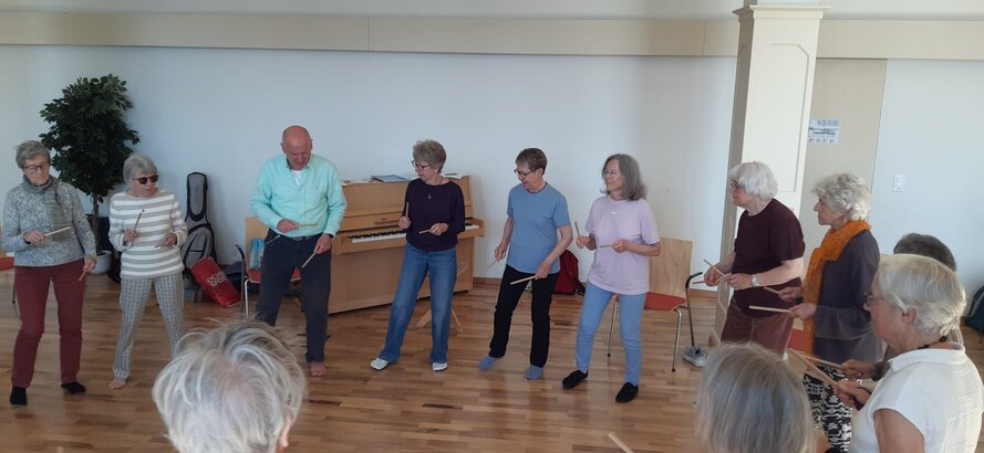 Rhythmik-Leiter spielt Klavier, während ältere Teilnehmende sich im Raum dazu bewegen.