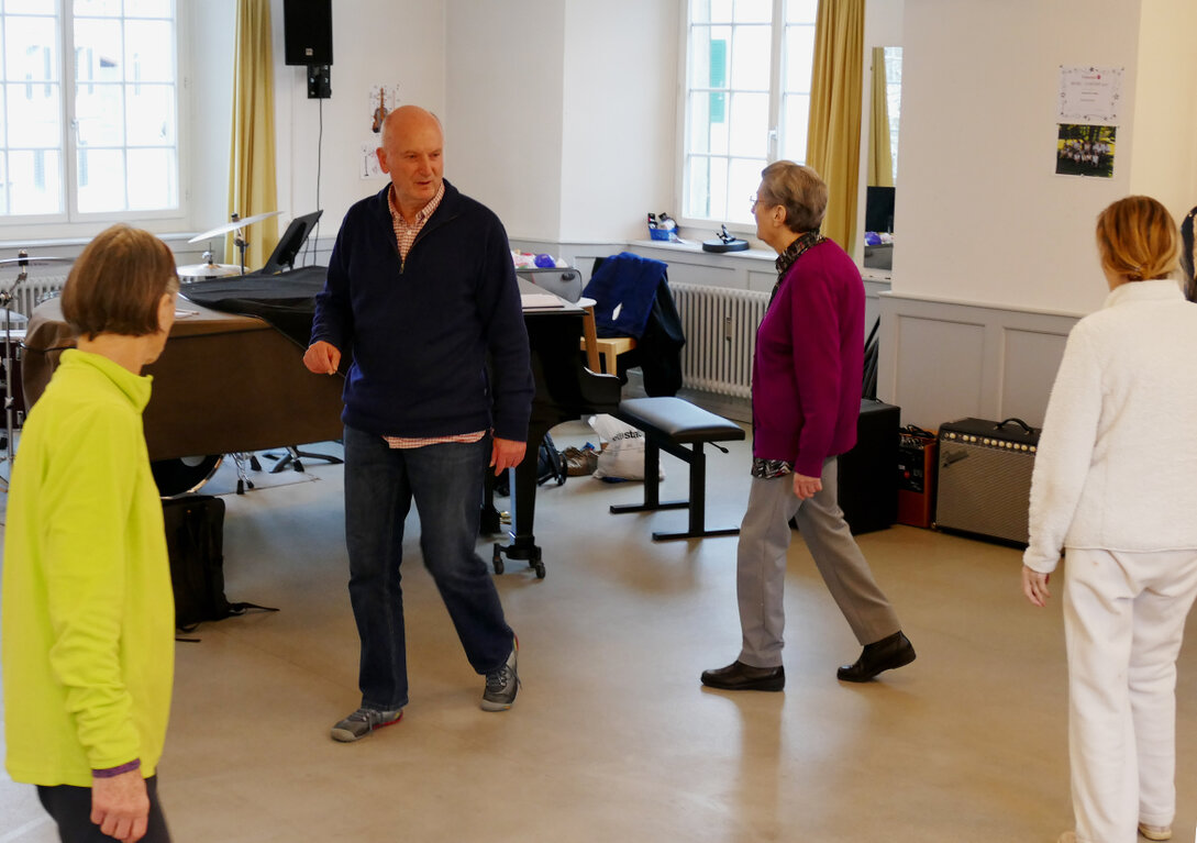 Ältere Menschen gehen gemeinsam im Takt der Musik durch einen Übungsraum.